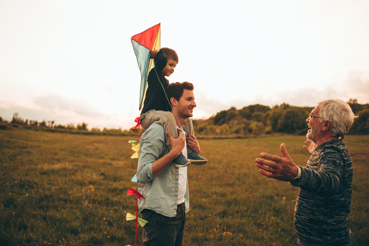 Photo of a three generations of men, who enjoy kite running and spending time together outdoors in the nature